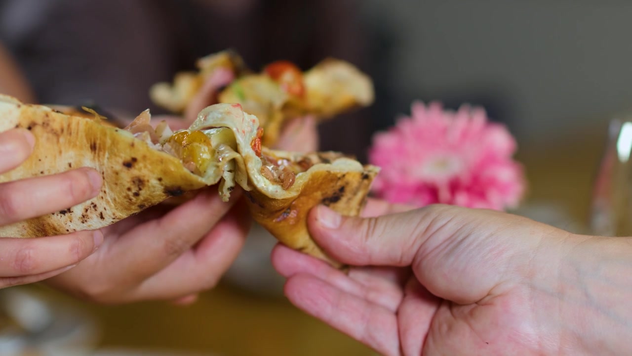 Primo piano di mani che condividono fette di pizza su un tavolo con vino e fiori