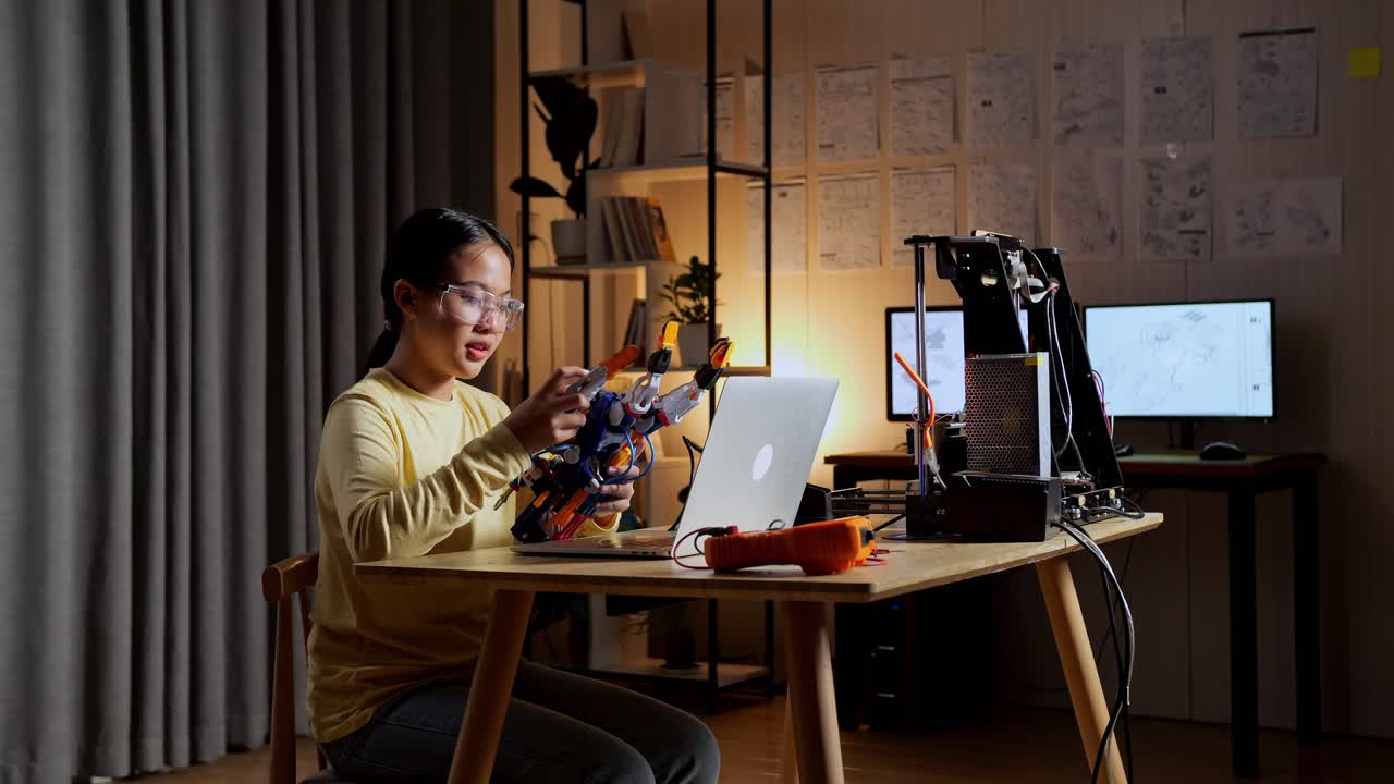 una adolescente asiática con una computadora portátil comprobando una mano de cyborg en casa