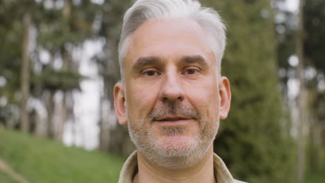 portrait of a gray haired man standing in the park and looking at the camera 2