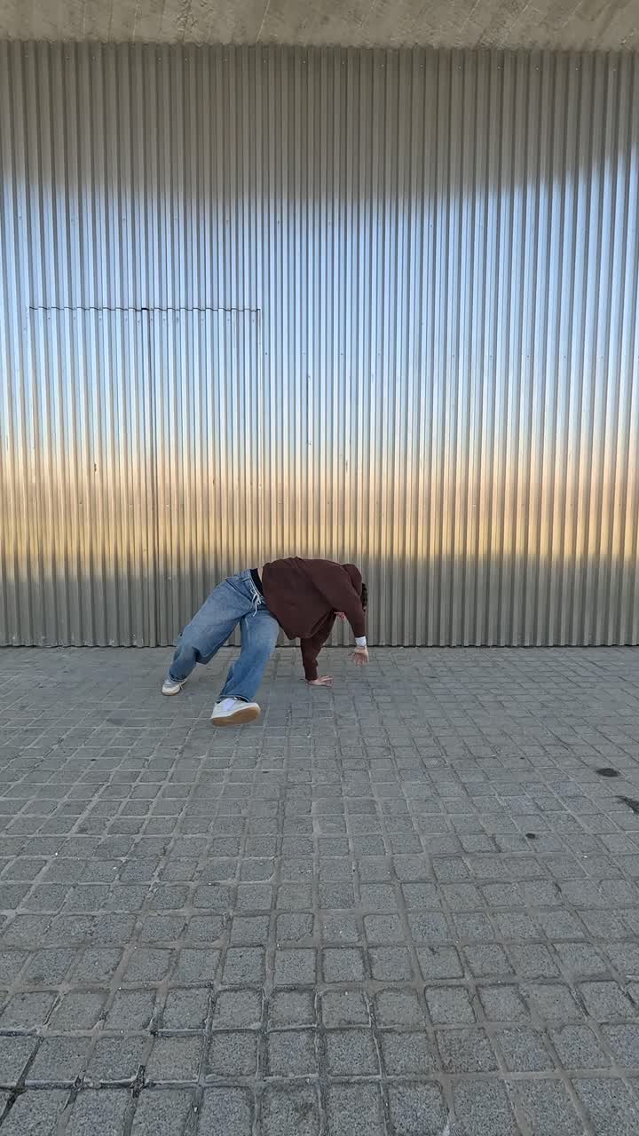Giovane ballerino energico che esegue passi di street dance contro una parete metallica
