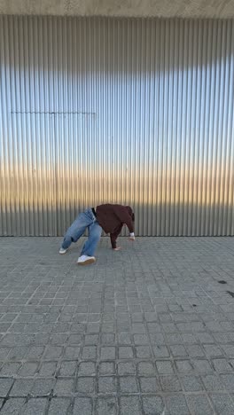 young energetic dancer performing street dance moves against metal wall