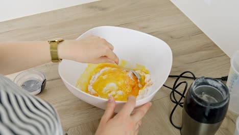 close-up of female caucasian hands mixing egg yolk and powdered sugar for tiramisu preparation.