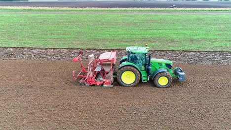 side view of a tractor and seed drill sowing wheat in a wet field.