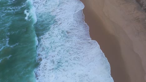 aerial view tilting over waves and alone women walking at the magoito beach, cloudy sunset in portugal