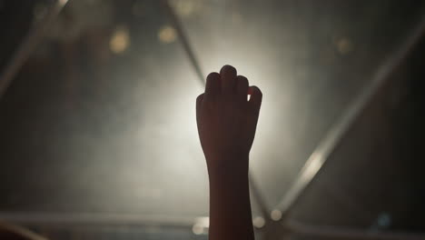 la mano de la mujer juega con el dedo en un primer plano en una habitación oscura. la silueta del brazo de la dama hace gestos elegantes contra una lámpara brillante en un espacio oscuro. señales de lenguaje corporal
