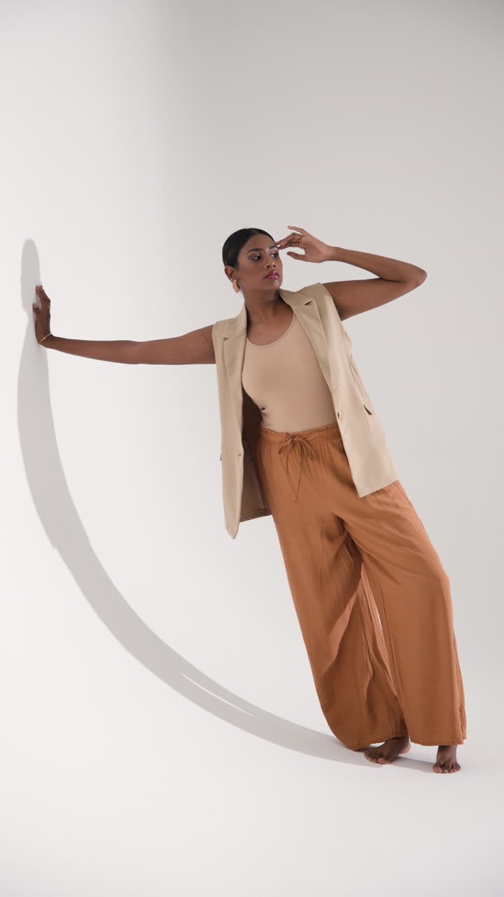 Vertical video: Model in stylish outfit posing gracefully against white wall in fashion studio