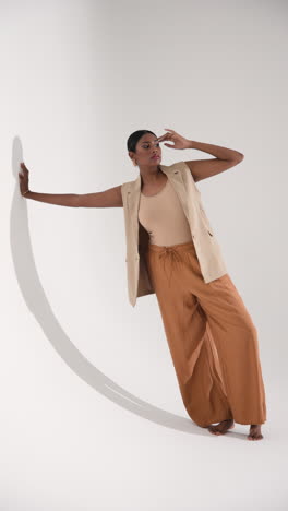 vertical video: model in stylish outfit posing gracefully against white wall in fashion studio