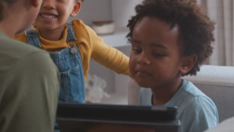 Mother-With-Children-Playing-Game-Or-Streaming-To-Digital-Tablet-Sitting-On-Sofa-At-Home-Together