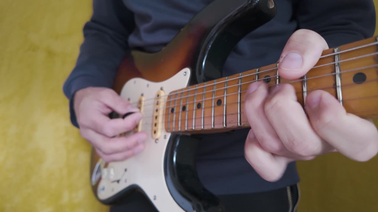 Close up view of hands skillfully playing a sunburst electric guitar, set against a vibrant yellow backdrop, capturing the essence of music