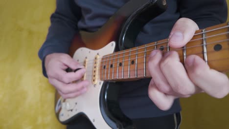 close up view of hands skillfully playing a sunburst electric guitar, set against a vibrant yellow backdrop, capturing the essence of music