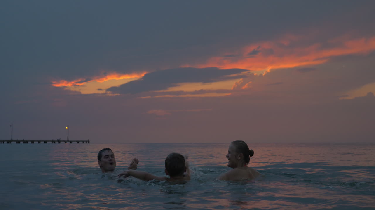 해가 지면 어머니와 아버지와 아들들이 그리스 페레아 시의 바다에서 수영하고 있다.