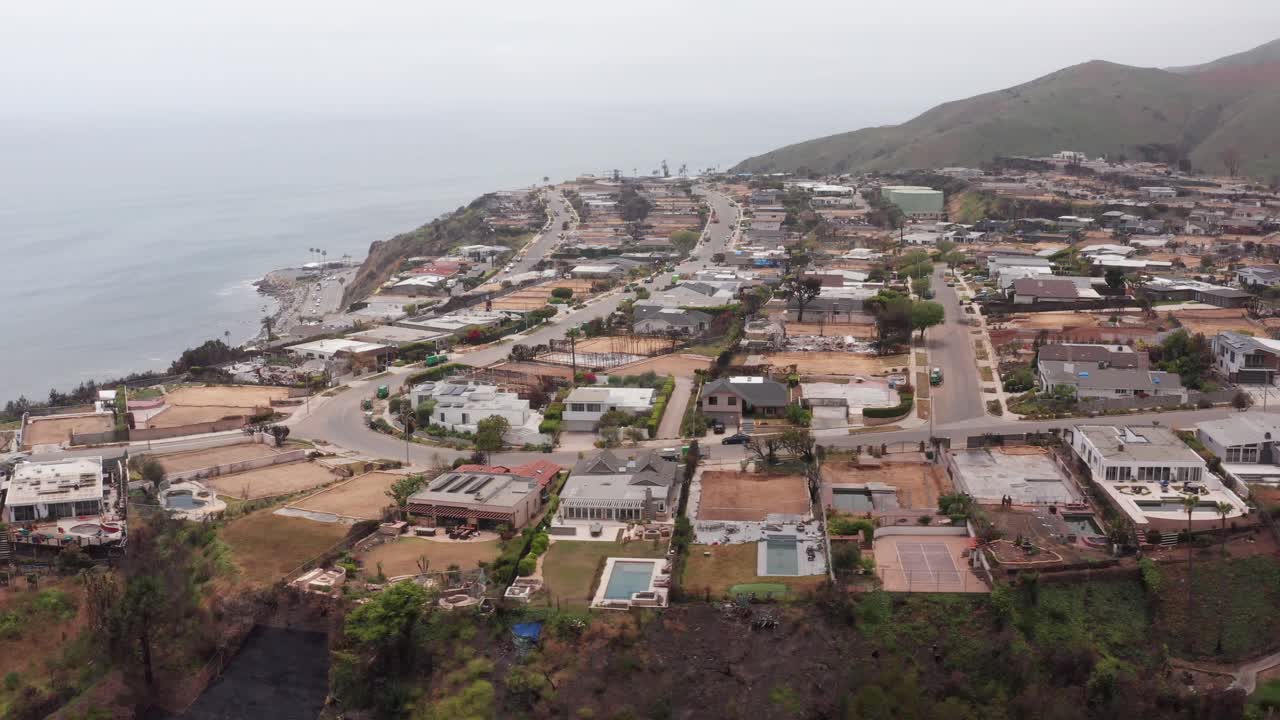 Descending aerial dolly shot of cleared residential lots in the oceanfront Sunset Mesa neighborhood after the Palisades Fire in Malibu, California. 4K