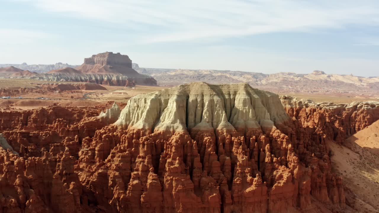 Gorgeous trucking right aerial drone shot of the beautiful Goblin Valley Utah State Park with pointy red hoodoo rock formations and red and white Butte's looming above on a warm sunny summer day