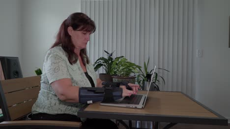 middle aged caucasian woman with carpal tunnel wraps on and typing on a computer with wide shot