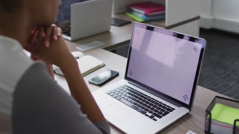 mujer de negocios de raza mixta sentada en un escritorio y usando una computadora portátil con espacio de copia en la pantalla en la oficina