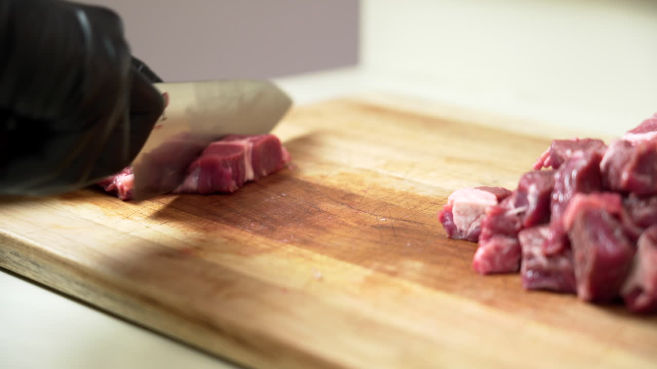 Koki Sedang Memotong Dadu Daging Sapi Chuck Segar Paling Lezat, Menggunakan Sarung Tangan Hitam dan Pisau Koki Tajam