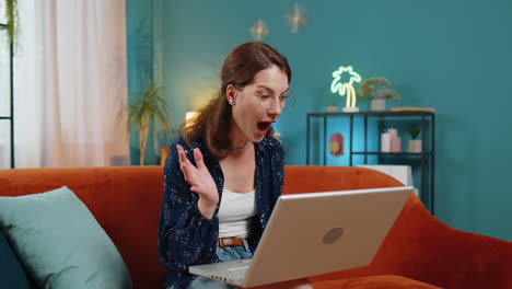 surprised happy young woman in eyeglasses using laptop computer receive good news message at home