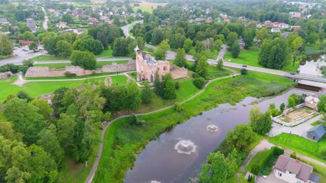 aerial view of dobele castle ruins, flowing berze river and illuminated fountains at sunset serene latvian summer evening from above, scenic aerial of latvian historical landscape in golden hour