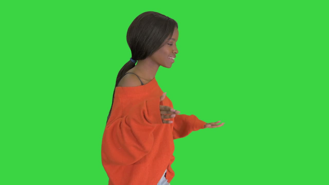 Relaxed african american young woman dressed in bright casual clothes dancing while walking on a Green Screen, Chroma Key