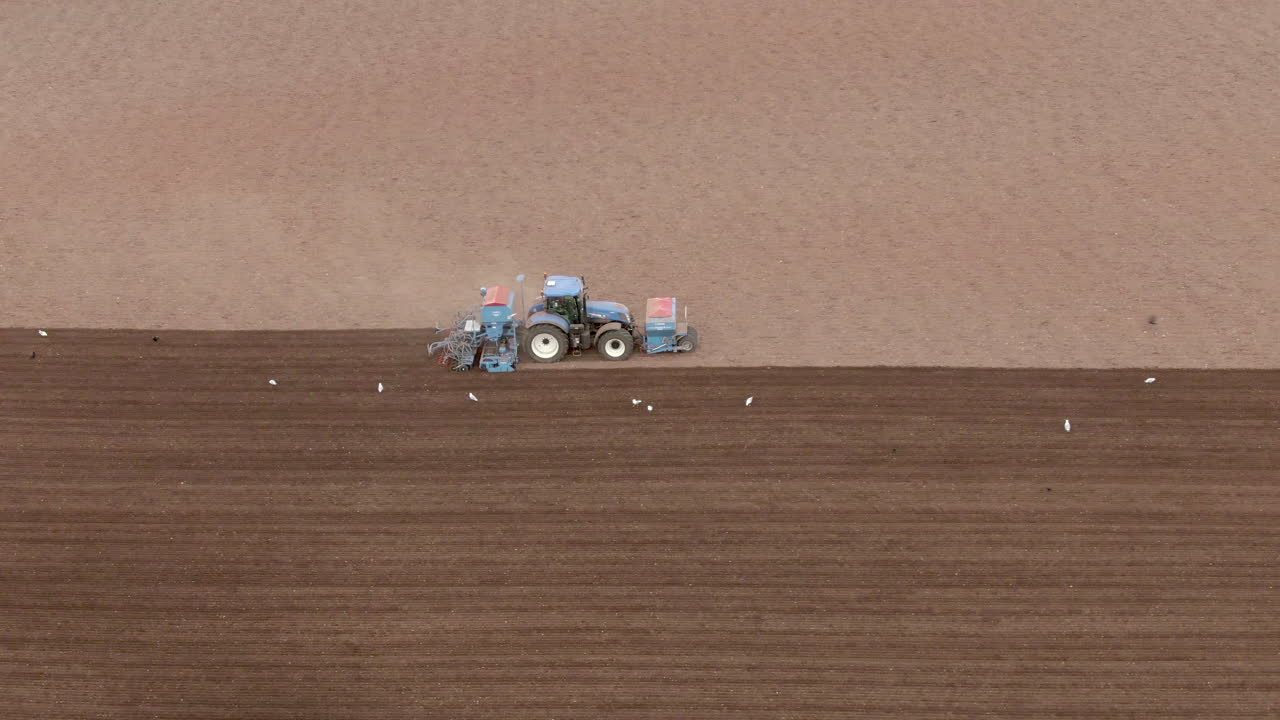 toma de seguimiento lateral aérea del lado derecho de un tractor mientras ara un campo, aberdeenshire, escocia