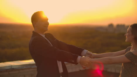 un hombre y una mujer enamorados bailan de pie en el techo de un edificio al atardecer mirándose el uno al otro.