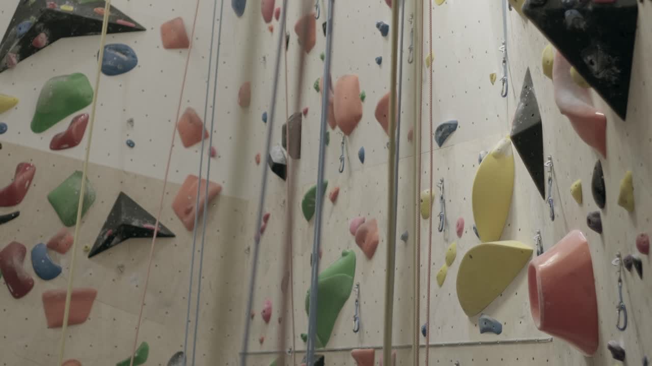 parede de escalada em rocha colorida com várias garras e cordas