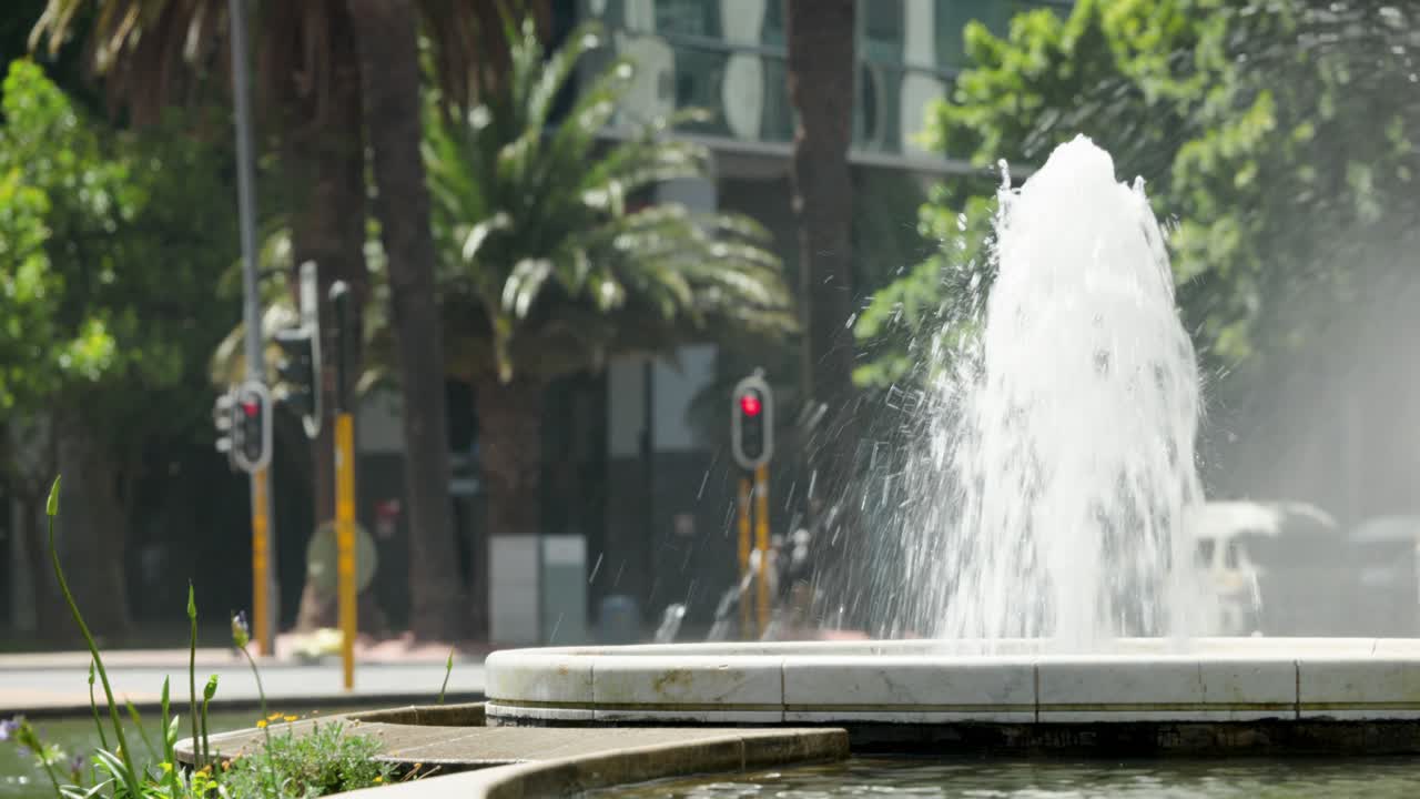 Personas diversas cruzando en una plaza de la ciudad, pasando una fuente de piedra y ocluyendo brevemente mientras se desplazan.