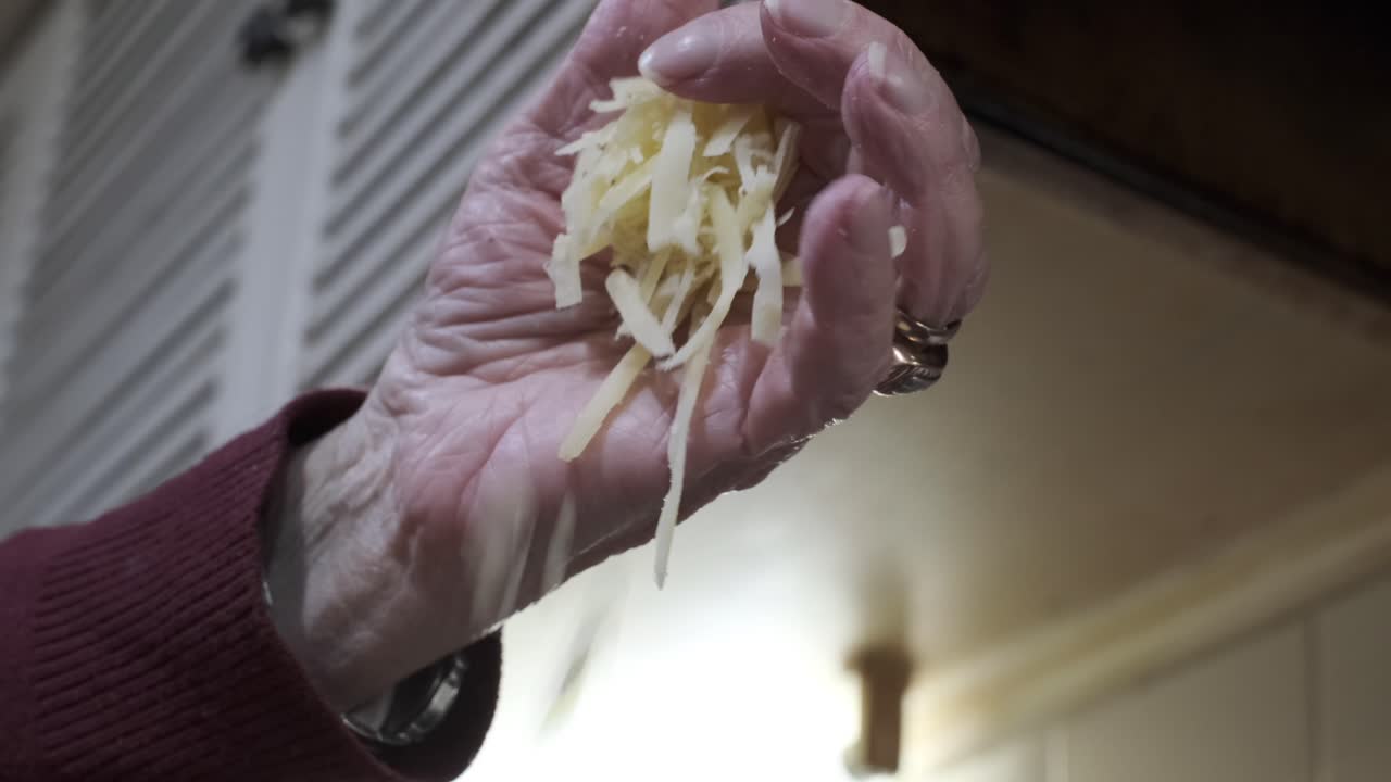 Beautiful hand drops shredded cheese onto fondue pot for melting, slow motion