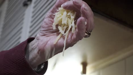 beautiful hand drops shredded cheese onto fondue pot for melting, slow motion