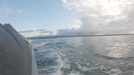 a bird flies close to the ocean while a boat moves away from an island. the panga creates waves on an ocean of the galapagos islands