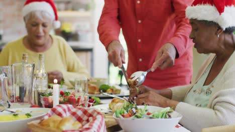 hombre caucásico mayor tallando y sirviendo pavo en la mesa de la cena de navidad con diversos amigos