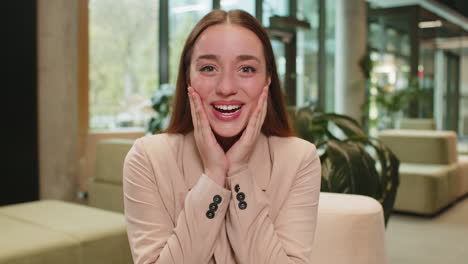 caucasian young businesswoman lady looking at camera shocked by sudden victory in office lobby