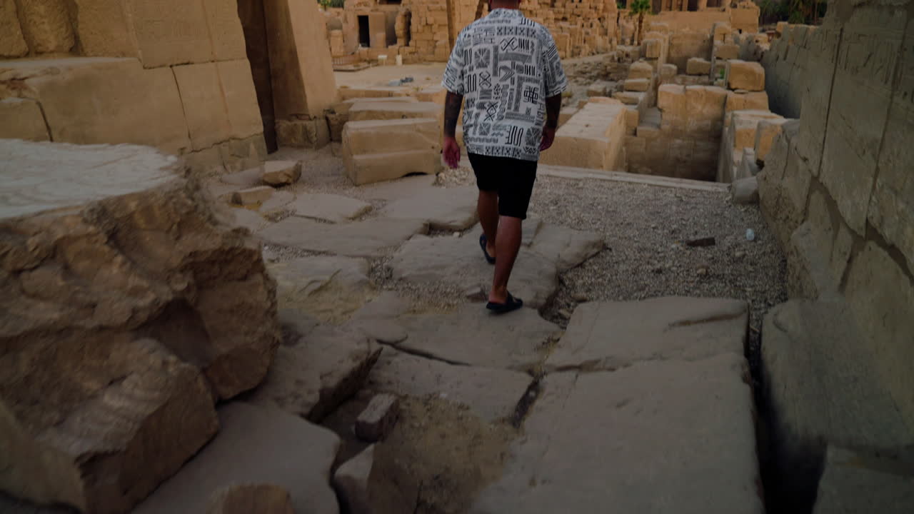 Man Walking At Karnak Temple Complex During Sunrise In Luxor, Egypt. rear view, tilt-up shot
