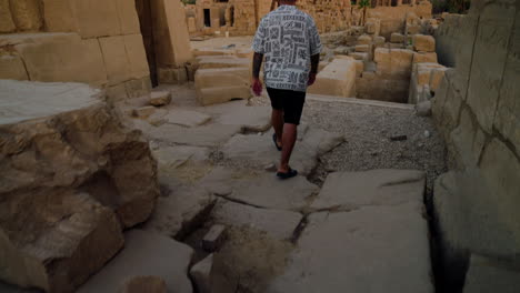 man walking at karnak temple complex during sunrise in luxor, egypt. rear view, tilt-up shot