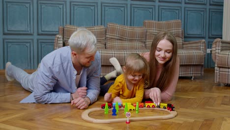 happy family playing with wooden train set on the floor