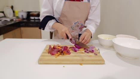 skilled lady chef cutting onion with sharp knife on wooden board in kitchen