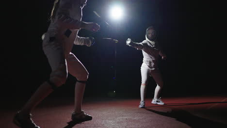 two young female fencers compete in an indoor arena