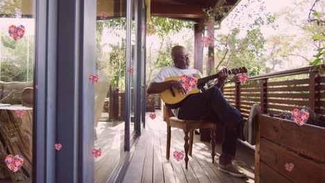 animation of pink flowers over senior african american man playing guitar on terrace at home