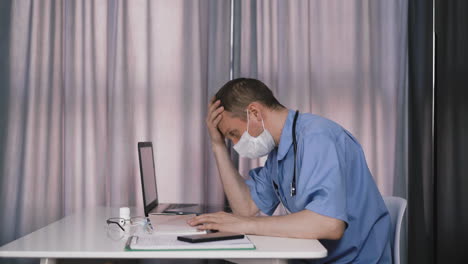 tired-doctor-in-uniform-reads-medical-records-at-table