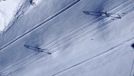 high aerial shot looking down on a lone snow skier casually carving left and right slaloming down a steep majestic mountain slope at val senales glacier, a popular ski resort, italy, europe