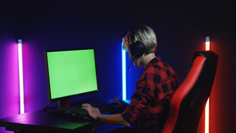 young woman playing on the computer with chroma key screen in a room with colorful neon lamps on the wall