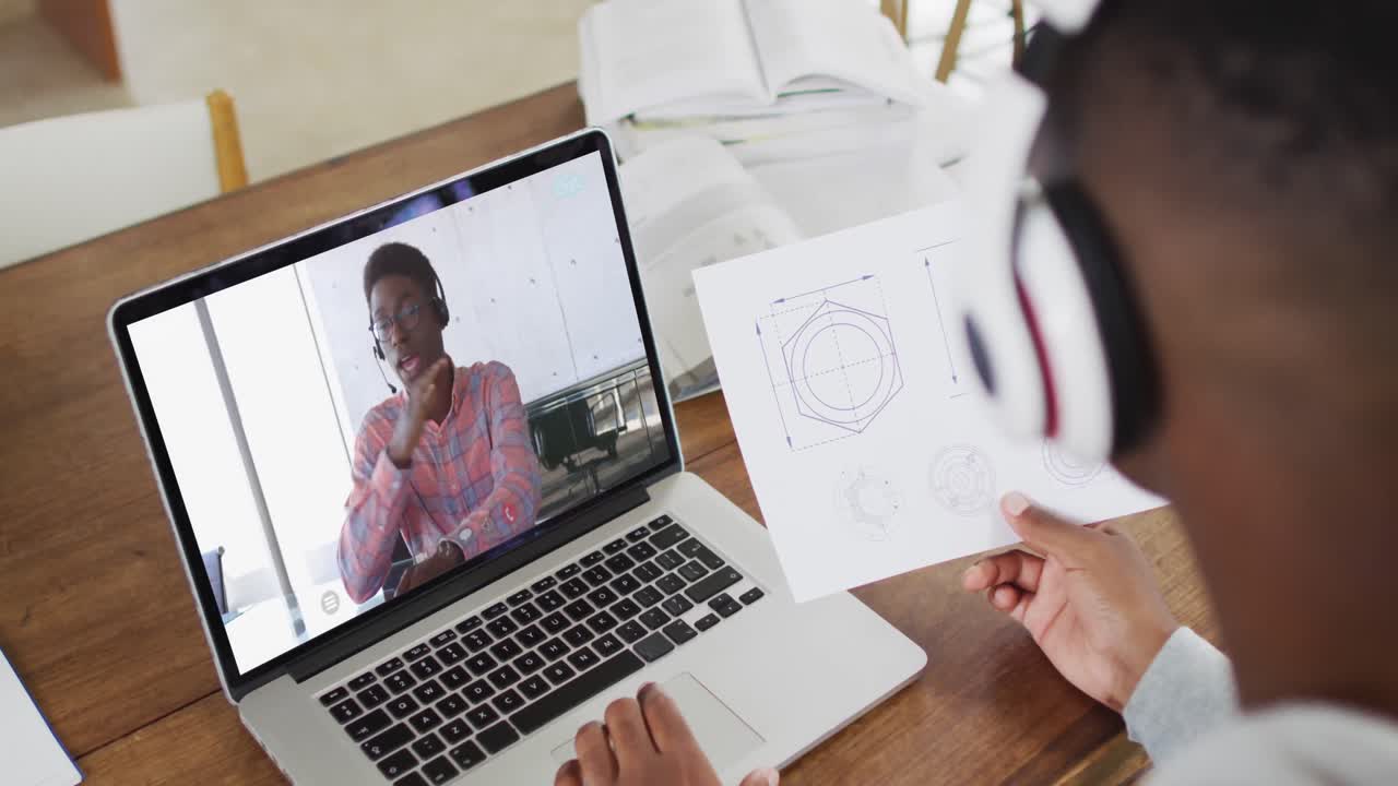 estudiante universitario afroamericano que sostiene notas mientras hace una videollamada en una computadora portátil en casa
