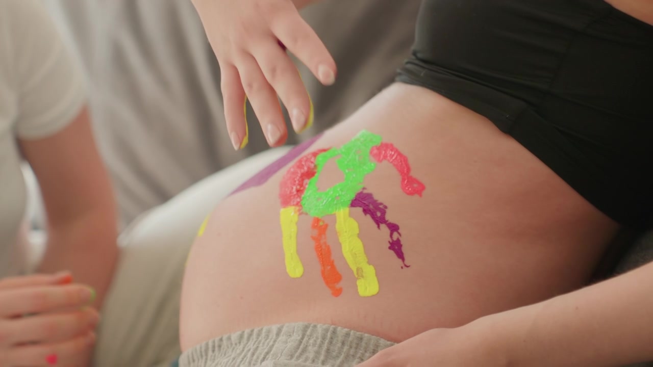 Primo piano di un'opera d'arte colorata con impronte di mani su una pancia di donna incinta