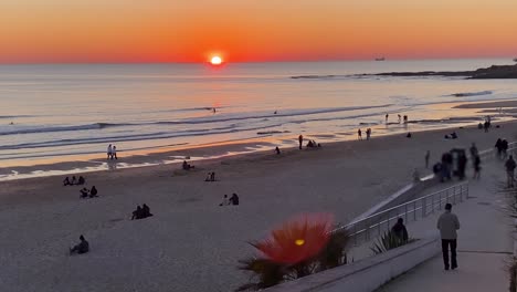 silhouettes of people walking on sandy beach and surfers at the sunset background on the atlantic coast of portugal