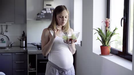 cheerful pregnant woman eating fresh salad at kitchen