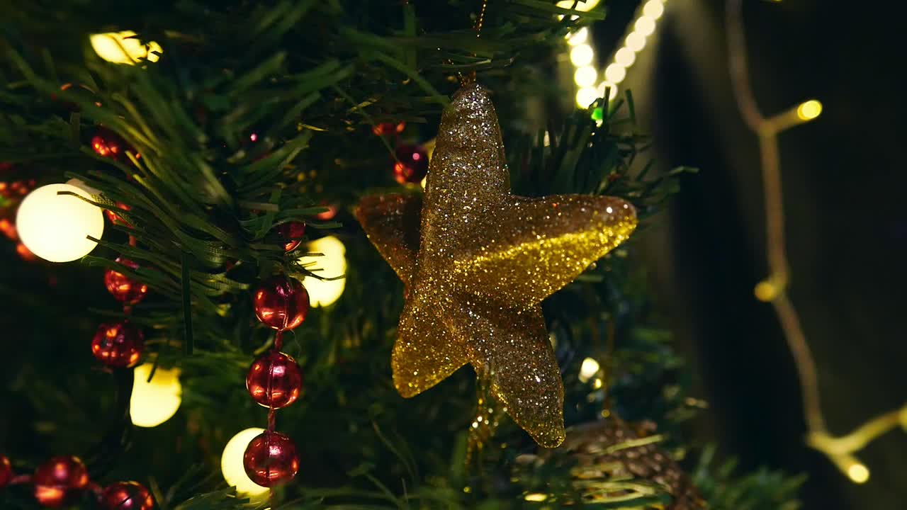 estrella dorada decorativa colgando del árbol de navidad con luz intermitente en el fondo, de mano