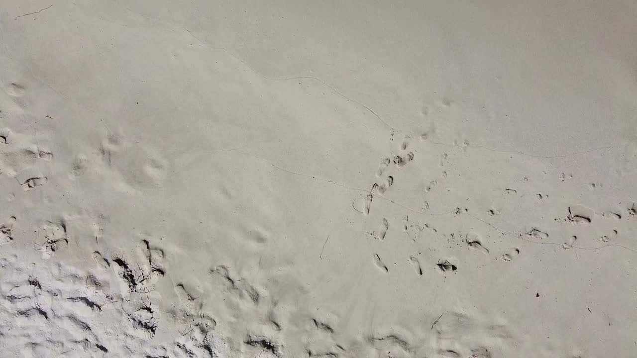 vista aérea de pájaro sobre una playa tranquila con huellas en la arena.