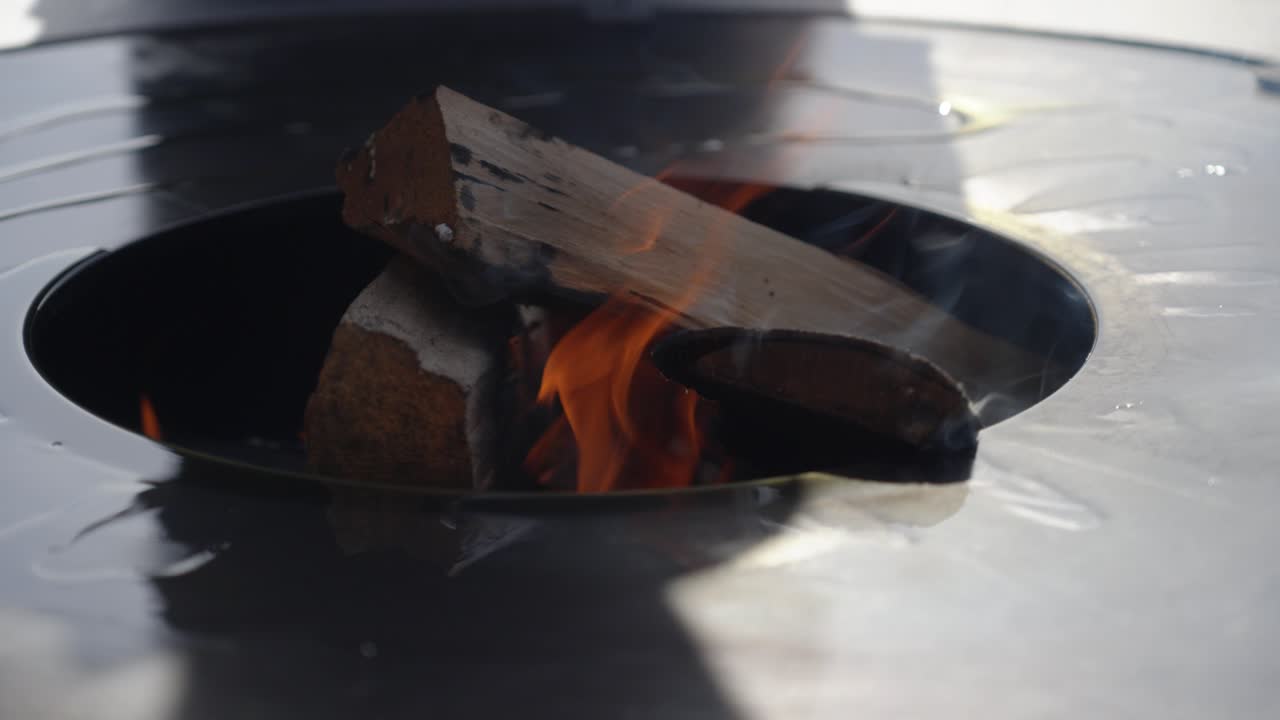oil being placed on a metal barbecue plate with wood log burning to cook