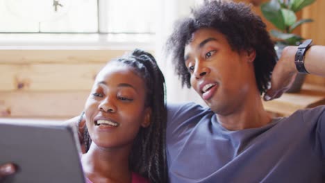 Happy-african-american-couple-using-tablet,-sitting-on-sofa-in-log-cabin,-slow-motion