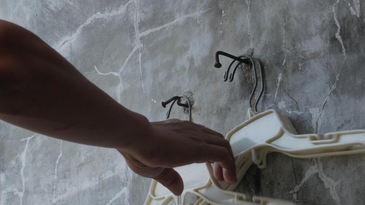 Hand Taking a Plastic Clothes Hanger from a Wall Hook
